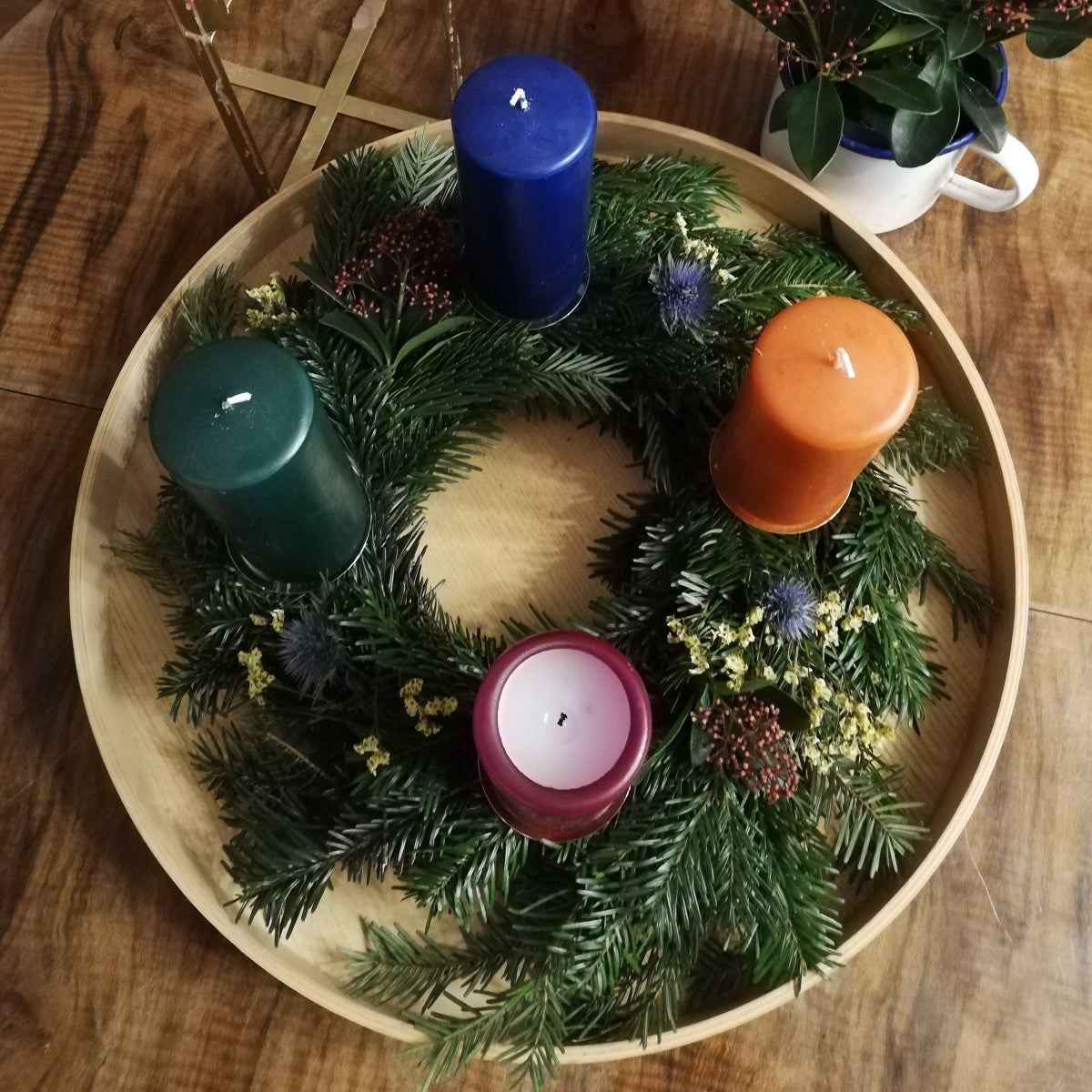 Bunter Adventskranz in Blau-, Rot- und Orangetönen auf einem Tablett, mit verschiedenfarbigen Kerzen dekoriert.
