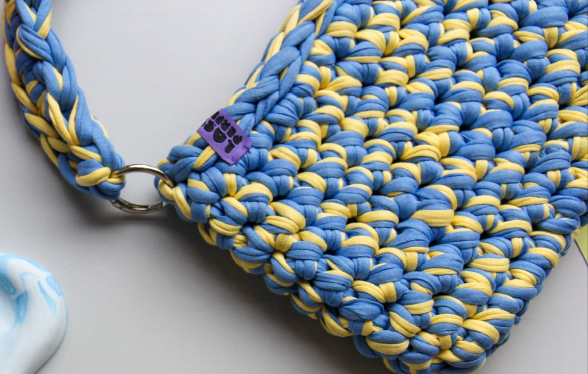 Selbstgemachte gehäkelte Tasche in Blau und Gelb aus einem Workshop, mit ‘Lost in Perfection’-Logo.