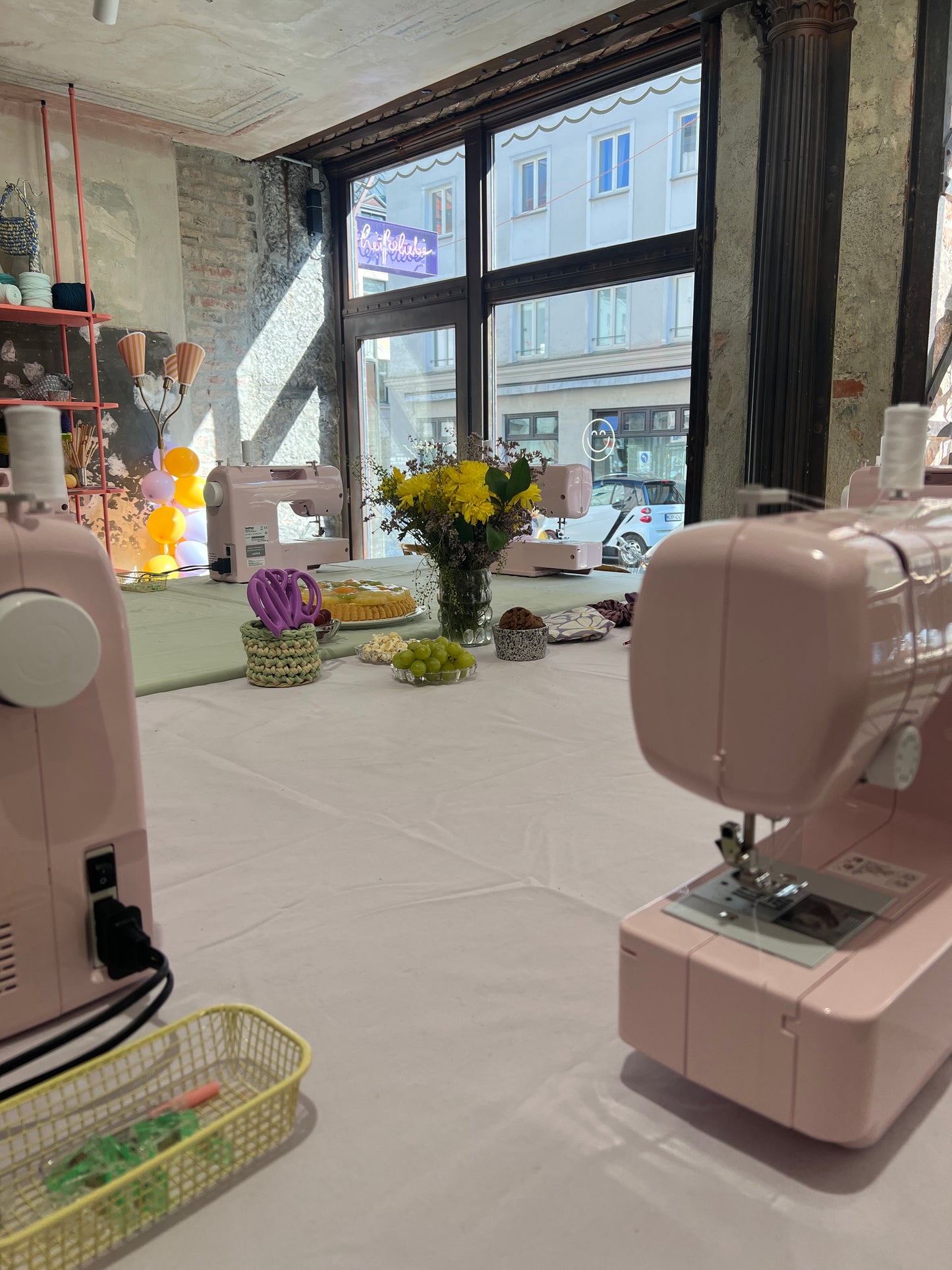 Nähen lernen von den ersten Stichen an. Workshop-Raum voller rosa Nähmaschinen, Garn, Blumen und Utensilien.