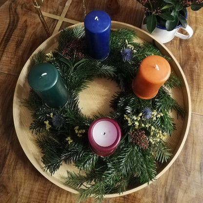 Bunter Adventskranz in Blau-, Rot- und Orangetönen auf einem Tablett, mit verschiedenfarbigen Kerzen dekoriert.