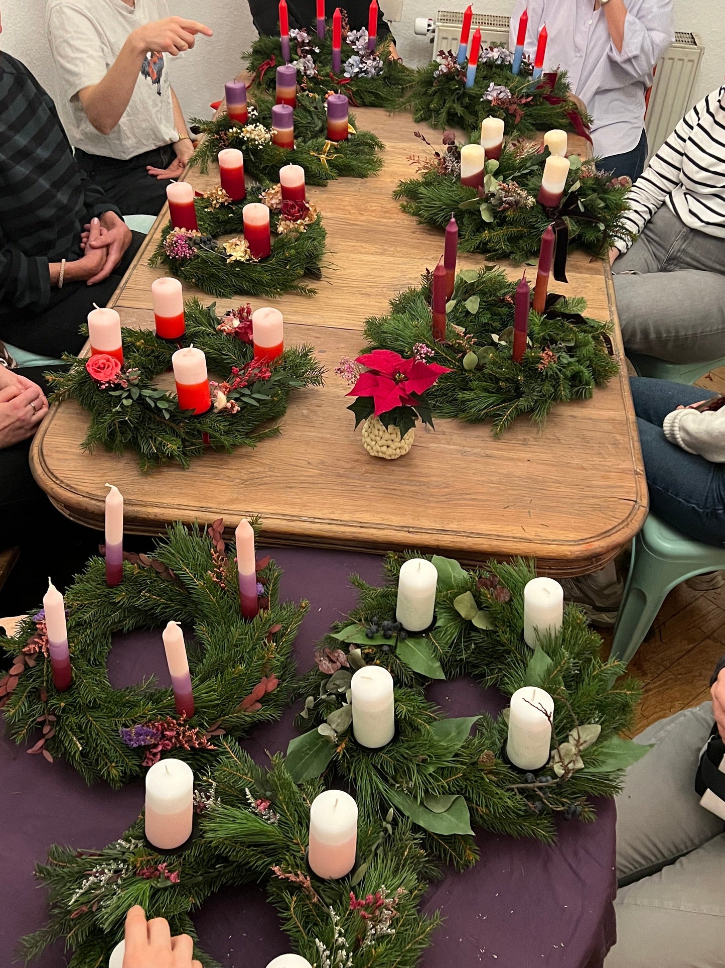 Tisch mit vielen Adventskränzen und bunten Kerzen.