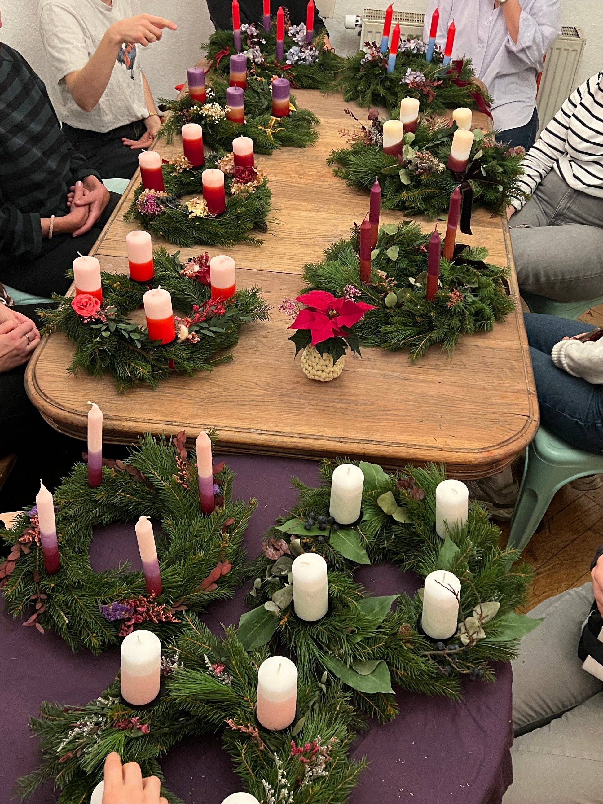 Tisch mit vielen Adventskränzen und bunten Kerzen.