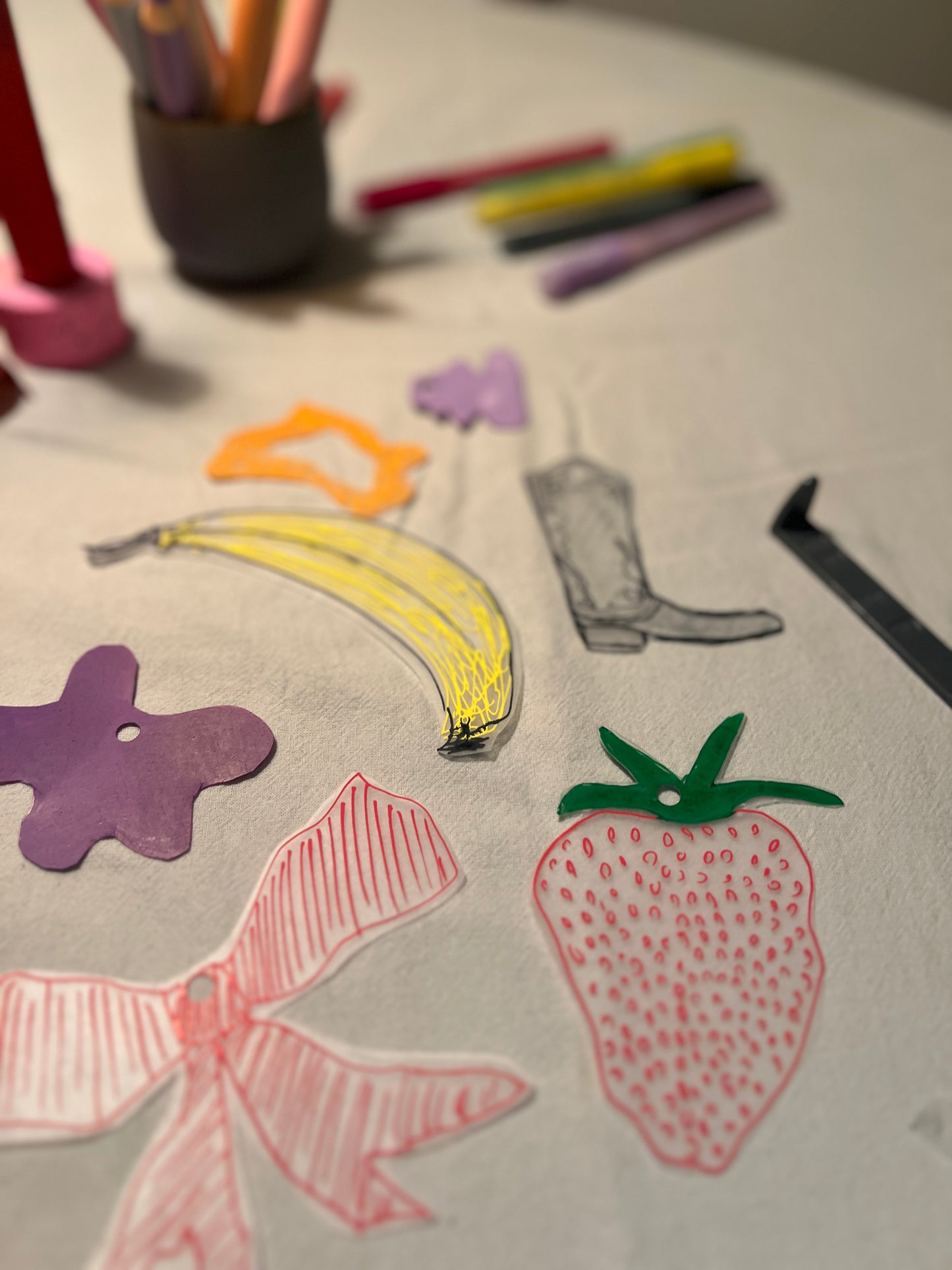 Schrumpffolien Motive wie Erdbeeren, Banane, Cowboystiefel auf dem Tisch für Schlüsselanhänger beim Workshop in München.