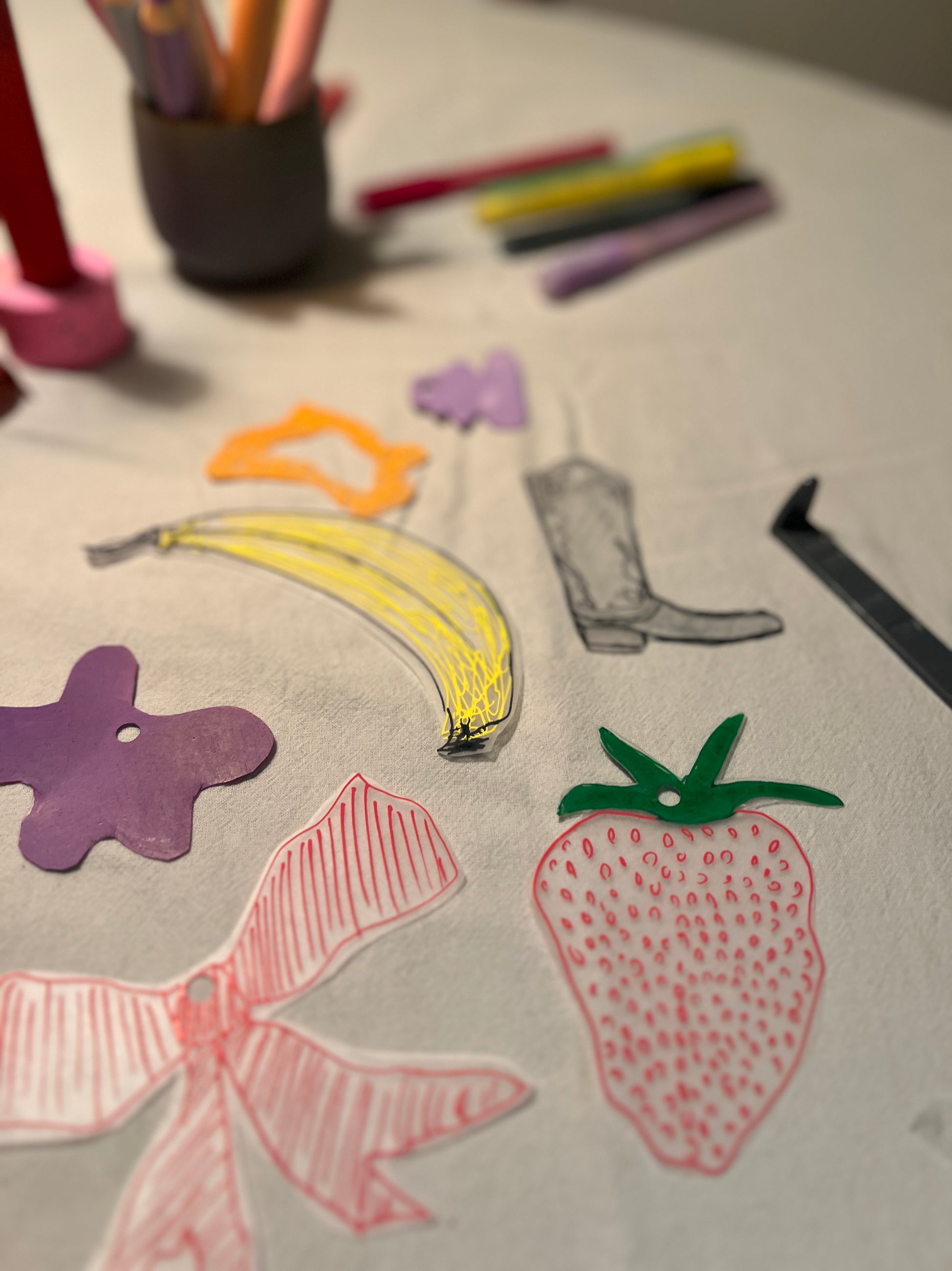 Schrumpffolien Motive wie Erdbeeren, Banane, Cowboystiefel auf dem Tisch für Schlüsselanhänger beim Workshop in München.
