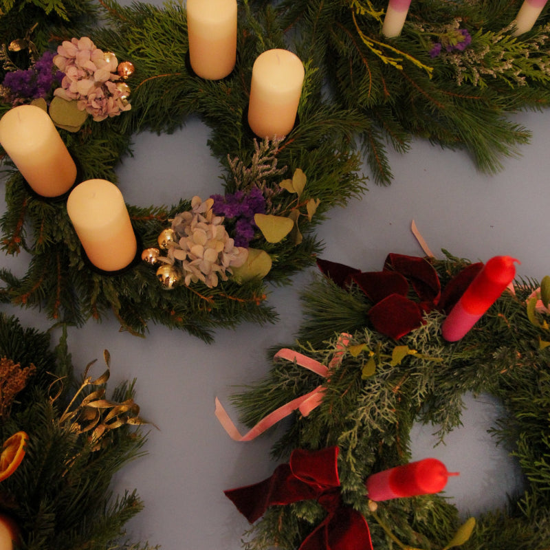 Adventskränze aus frischen Tannengrün, Trockeblumen, Samtbändern und Kerzen.